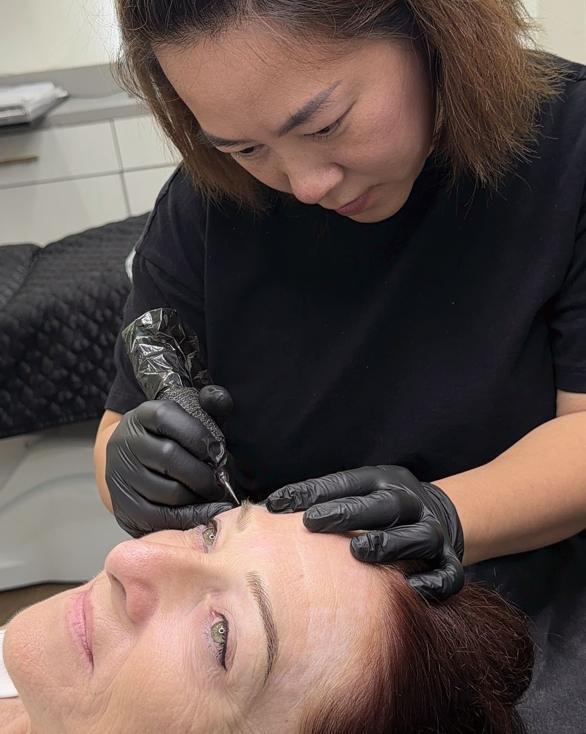 Artist working on a client's brows with a permanent makeup machine